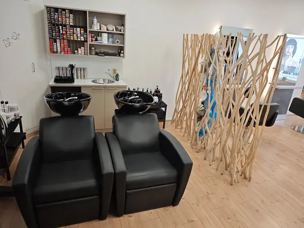 Moderner Friseursalon mit zwei schwarzen Waschsesseln, Holztrennwand und Farbauswahl.